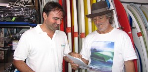 Y Carlos que llevaba grabada la ola de los comienzos en su camiseta, me acogió con cariño e ilusión. Y yo además le traje un regalo. Una foto que había estado oculta 33 años en un álbum de fotos en la otra parte de la península. Una foto en la que sale él, su coche y su perra. Una imagen que volvía al lugar de origen, donde se había tomado, Cantabria: Casa Lola. Una foto tomada por el pionero malagueño Javier Gabernet y que gracias a él y a esta investigación salió por fin a la luz. Obsérvese la cara de sorpresa, alegría y añoranza, tal vez por su fiel animalito que asomaba la cabeza por la ventana del coche (no soy traductor de pensamientos, tan solo es lo que creo que está reflejando Carlos al mirar la foto). Estuvimos un ratazo hablando de muchas cosas. A la antigua, como solía ocurrir en las tiendas de surf antes de la llegada del ciberespacio, ahora ya se ve menos, el concepto de tienda de surf no como lugar únicamente de compra, sino de adquisición de conocimiento, de charlas y debates. Gracias Carlos. 